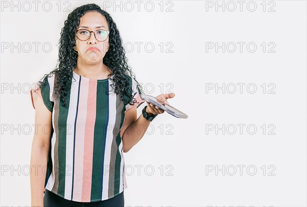 Indifferent girl holding cell phone isolated. Young skeptical woman with cell phone in hand isolated. Sad woman with cell phone looking at camera