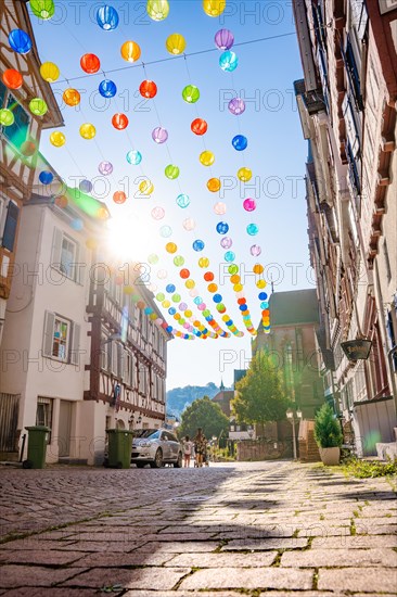 Colourful lanterns hanging in alleyway alley between half-timbered houses