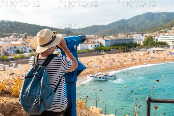 Elder tourist looking the landscape through coin operated binoculars standing on a viewpoint in the coastline