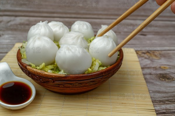 Xiao long bao of prawns on a bed of lettuce in a wooden bowl with chopsticks and a ceramic spoon with soy sauce