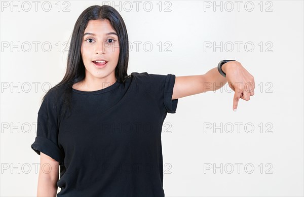 Amazed latin girl pointing down an advertisement. Cheerful girl pointing advertising down. Latin people pointing down at a banner