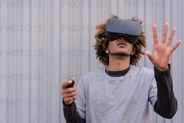 Horizontal photo with urban grey background of a street style young man gesturing while using virtual reality goggles