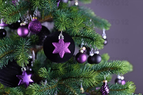 Close up of star shaped purple glass tree ornament bauble with decorated Christmas tree with other seasonal tree ornaments on dark gray background