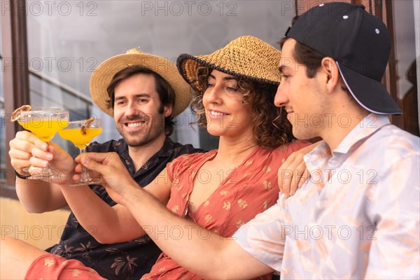 Casual three caucasian friends toasting rwith cocktails relaxed sitting on a terrace