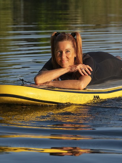 Woman lying relaxed on standup paddle board in lake