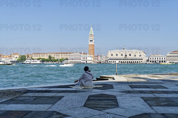 Woman having a picnic in the square in front of the church of San Giorgio Maggiore on the Giudecca Canal with a view of the Doge's Palace