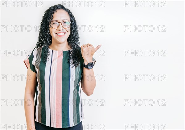 Smiling latin people pointing to a banner to the side. Happy latin woman recommending with fingers isolated. Cheerful curly haired girl pointing an offer