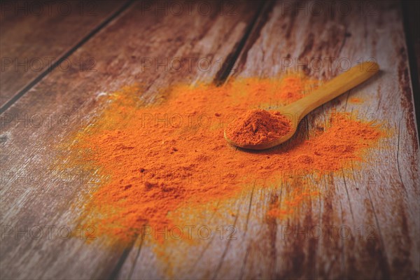 Ground turmeric in a wooden spoon poured on a wooden table with copy space