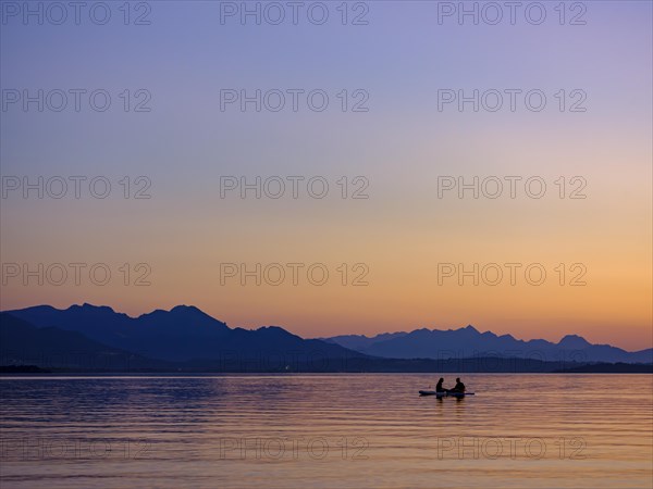 Two people sitting on their board in the water at dusk