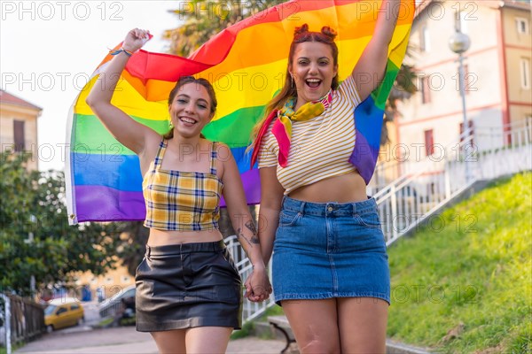 A closeup shot of two young Caucasian hugging females with LGBT pride flag outdoors