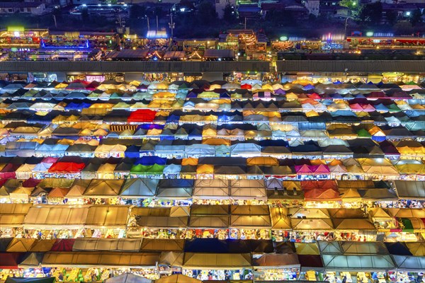 View of rows of colorful outdoor market tents and food stalls at night. Fairs