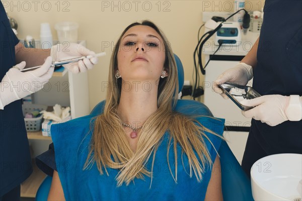 Beautiful young woman doing tooth examination in the dental office. Portrait of serious girl on a dental chair in dentistry