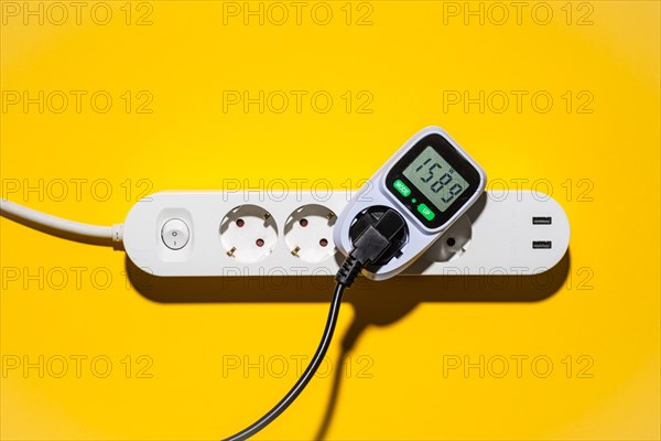 Top view of an energy cost meter in a power strip against a yellow background