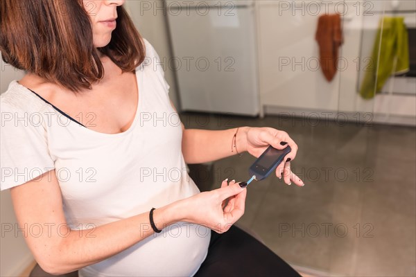 Young pregnant woman performing a gestational diabetes self-test to control sugar. Bleeding blood from his finger with a prick