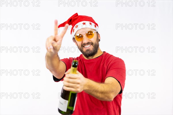 Young very happy Caucasian man with red Christmas hat toasting with a bottle of champagne on a white background