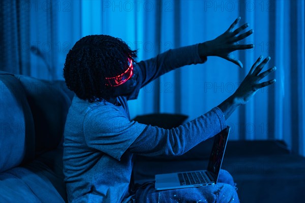 Afro man playing with laptop and Augmented reality goggles in a living room with neon blue light