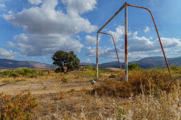 Old rusty soccer goal in an overgrown field with a broken soccer ball in front of it