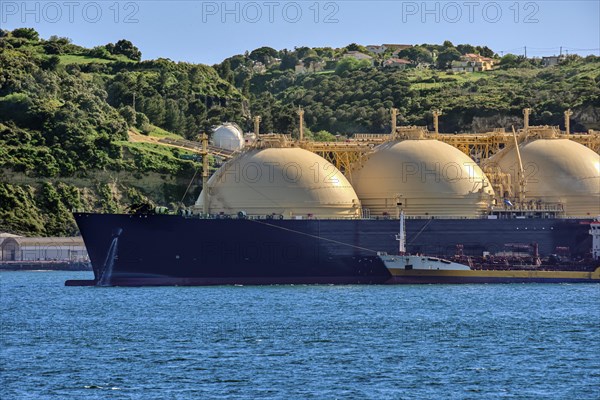 LNG or liquified natural gas tanker moored by industrial pier and green hill on sunny day. Alternative gas supply