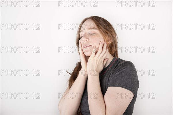 Beauty face. Smiling red haired woman touching healthy skin. Beautiful happy model with moisturized shiny fresh facial skin on white background in studio