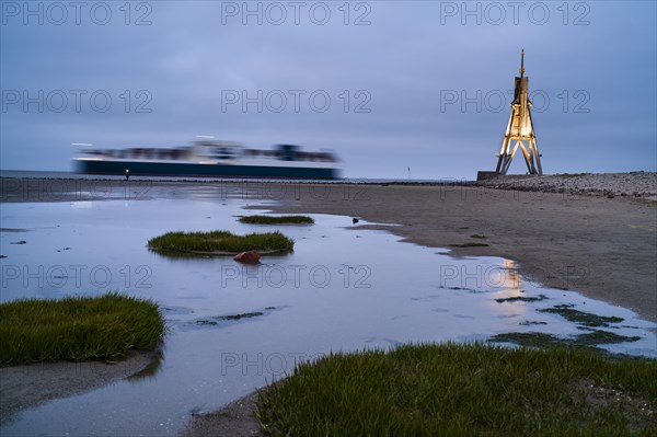 Kugelbake illuminated with cargo ship at dusk