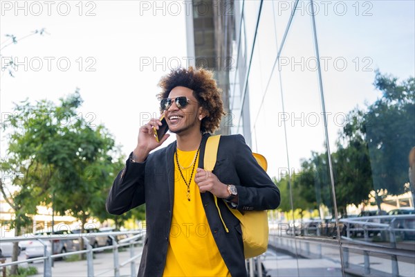 Casual stylish african american man talking to the phone while commuting with a bag