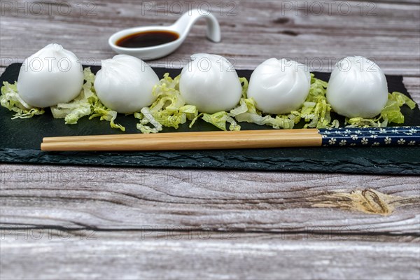 Xiao long bao of prawns on a bed of lettuce on a slate plate with chopsticks and a ceramic spoon with soy sauce