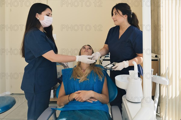 Female dentist with a help of her assistant fixing teeth of a woman patient in the dentists chair. Dentist examining patient teeth and having a dental checkup at dental clinic