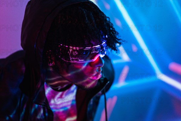 Studio portrait with purple and blue neon lights of an afro futuristic man wearing artificial intelligence goggles