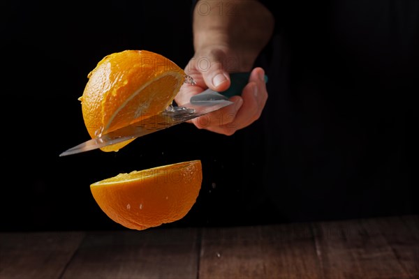 Woman cutting an orange in half with a knife in the air spilling water