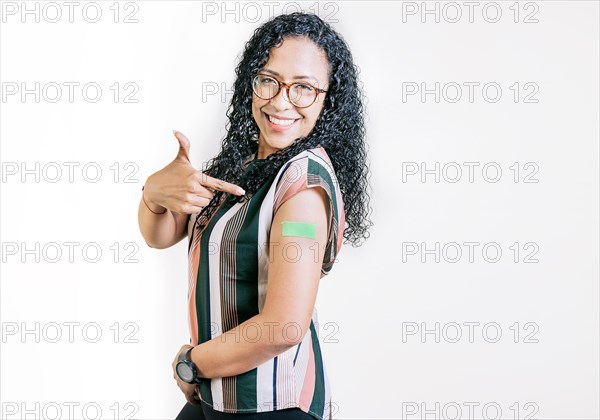 Smiling woman pointing at her vaccinated arm. Latin woman pointing at the bandage on her vaccinated arm