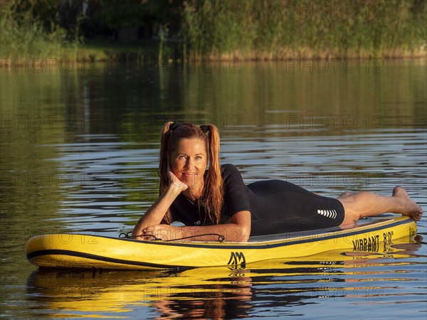 Woman lying relaxed on standup paddle board in lake