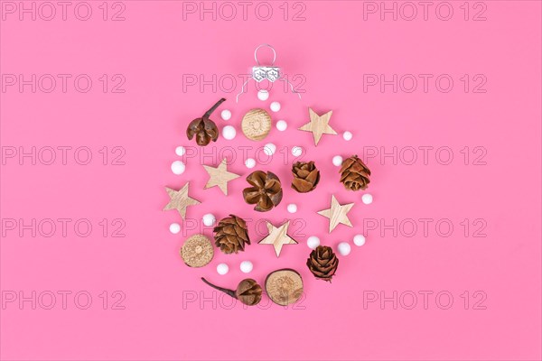 Seasonal ornaments like natural hernlock cones and stick slices with stars and white snowballs forming shape of Christmas tree bauble on pink background