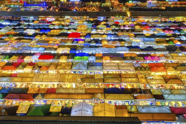 Close-up view of rows of colorful outdoor market tents and food stalls at night. Fairs