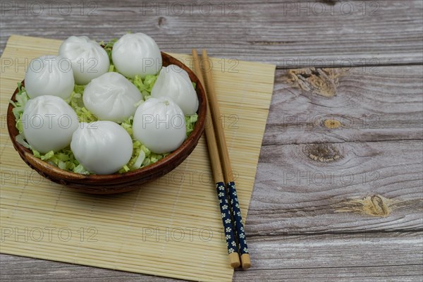 Xiao long bao of prawns on a bed of lettuce in a wooden bowl with chopsticks and a ceramic spoon with soy sauce