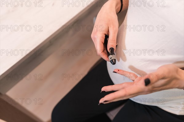 Young pregnant woman performing a gestational diabetes self-test to control sugar. Bleeding blood from his finger with a prick