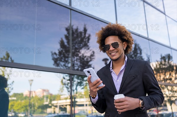 Cool businessman with sunglasses using phone standing in a financial district