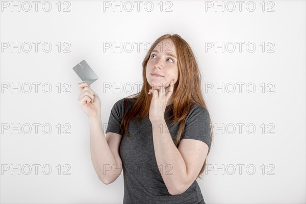 Thoughtful young red haired woman 20s in gray casual clothes isolated on white background studio portrait. People sincere emotions lifestyle concept. Copy space. Hold credit bank card