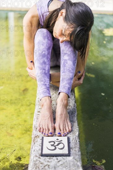 Aesthetic shot of a woman sitting behind an Om sign on a tree trunk over the water