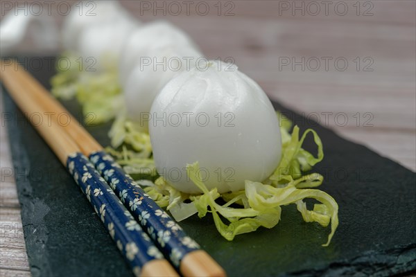 Xiao long bao of prawns on a bed of lettuce on a slate plate with chopsticks and a ceramic spoon with soy sauce