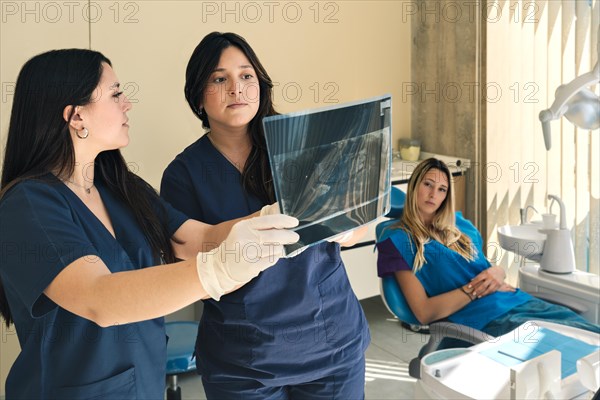 Dentist and assistant holding an x-ray and patient watching sitting in dental office chair