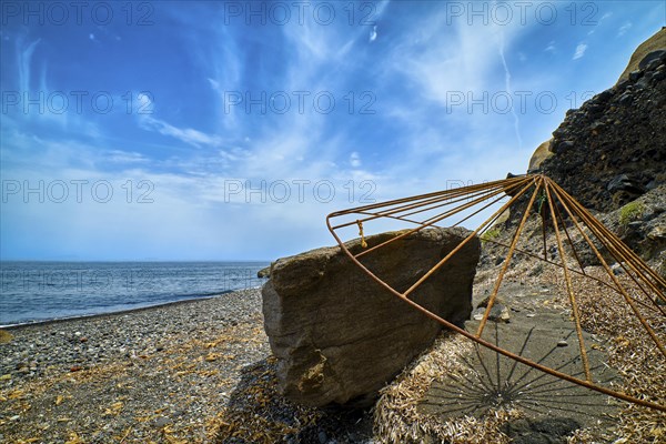 Rusty beach parasol carcass or frame resting on rock