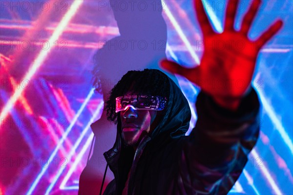 Studio portrait with purple and blue neon lights of a man raising hand wearing futuristic goggles