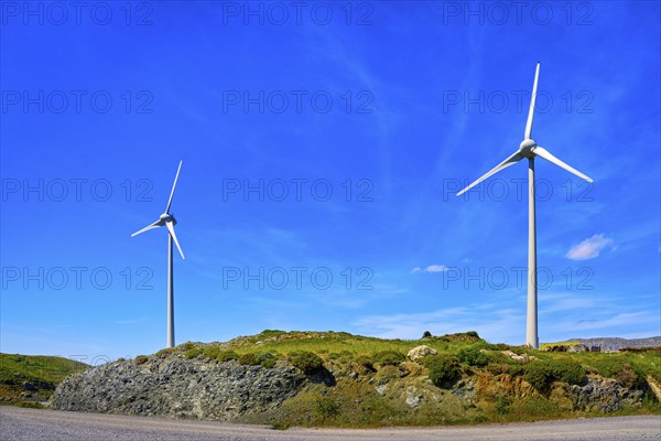 Two wind turbines on top of green hill on sunny day. Local energy production