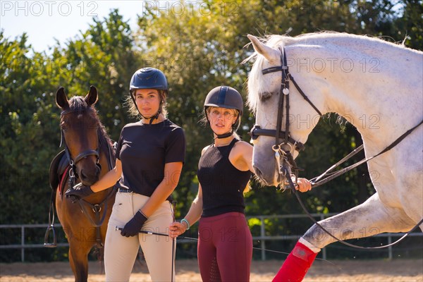 Two young Caucasian girl riders smiling next to their white and brown horses on a horse