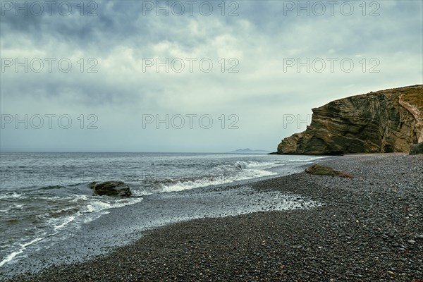 Dramatic landscape of stormy sea or ocean waves rolling on rocky volcanic beach on cloudy day. Overcast sky