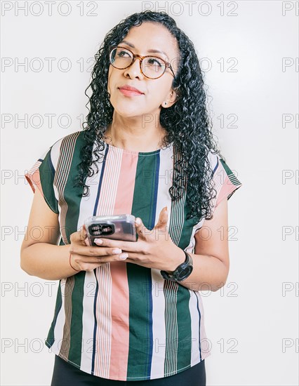Thoughtful young woman in glasses holding cell phone isolated. Pensive latin girl holding smart phone isolated