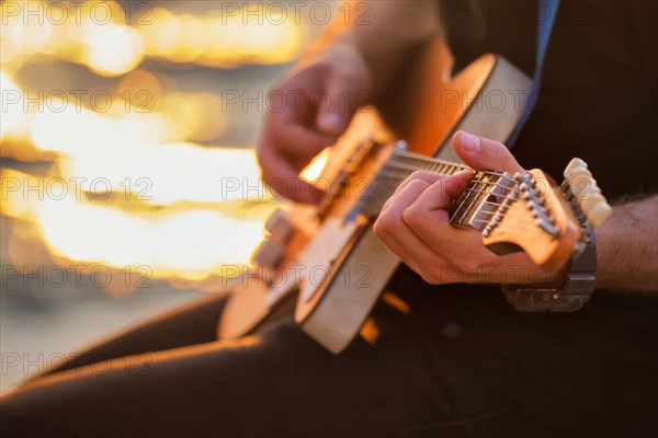 Street musician playing electric guitar hands with guitar pick close up with water in background