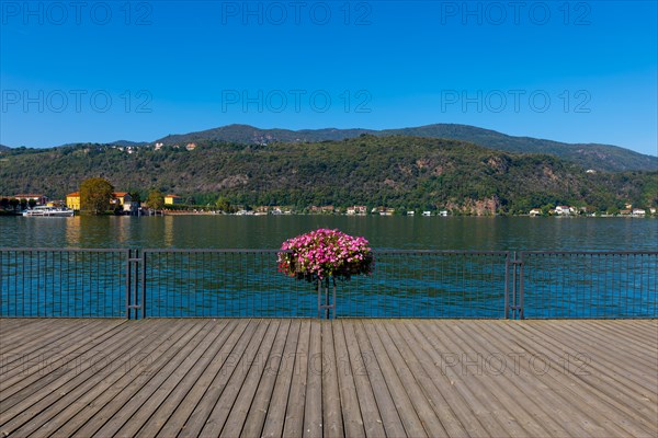 Elevated Walkway with Flowers on the Railing on Lake Lugano with Mountain in a Sunny Summer Day in Porto Ceresio