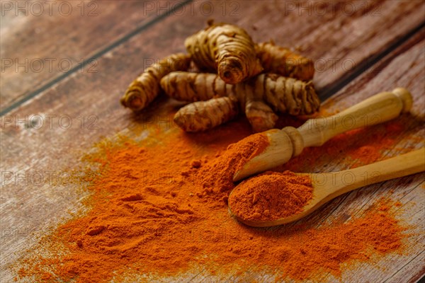 Fresh turmeric root and ground turmeric in a wooden spoon poured out on a wooden table