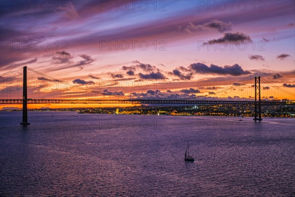 View of 25 de Abril Bridge famous tourist landmark of Lisbon connecting Lisboa and Almada on Setubal Peninsula over Tagus river in the evening twilight with boats. Lisbon